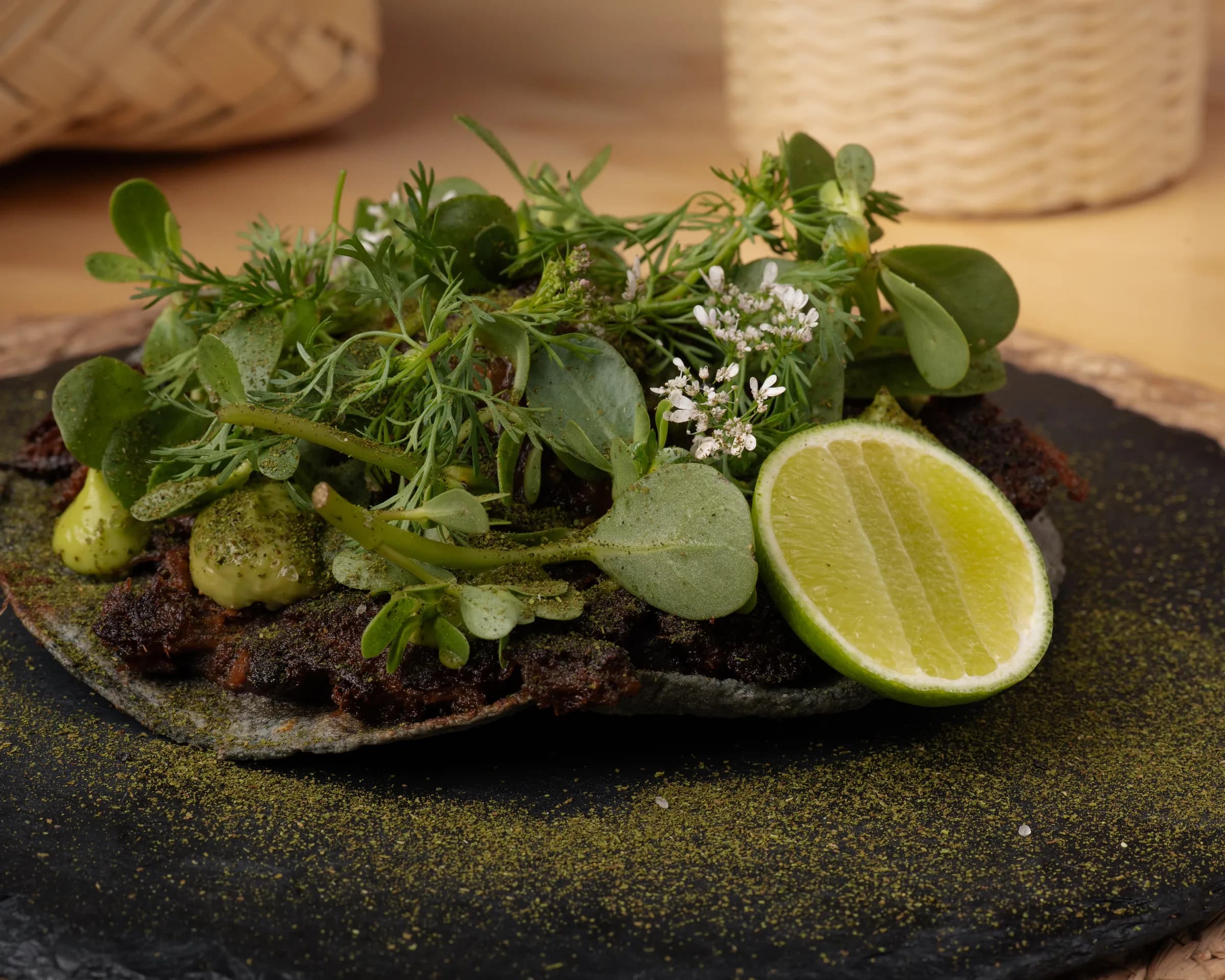 Tortilla oscura con carne, aguacate, hojas verdes y limón.