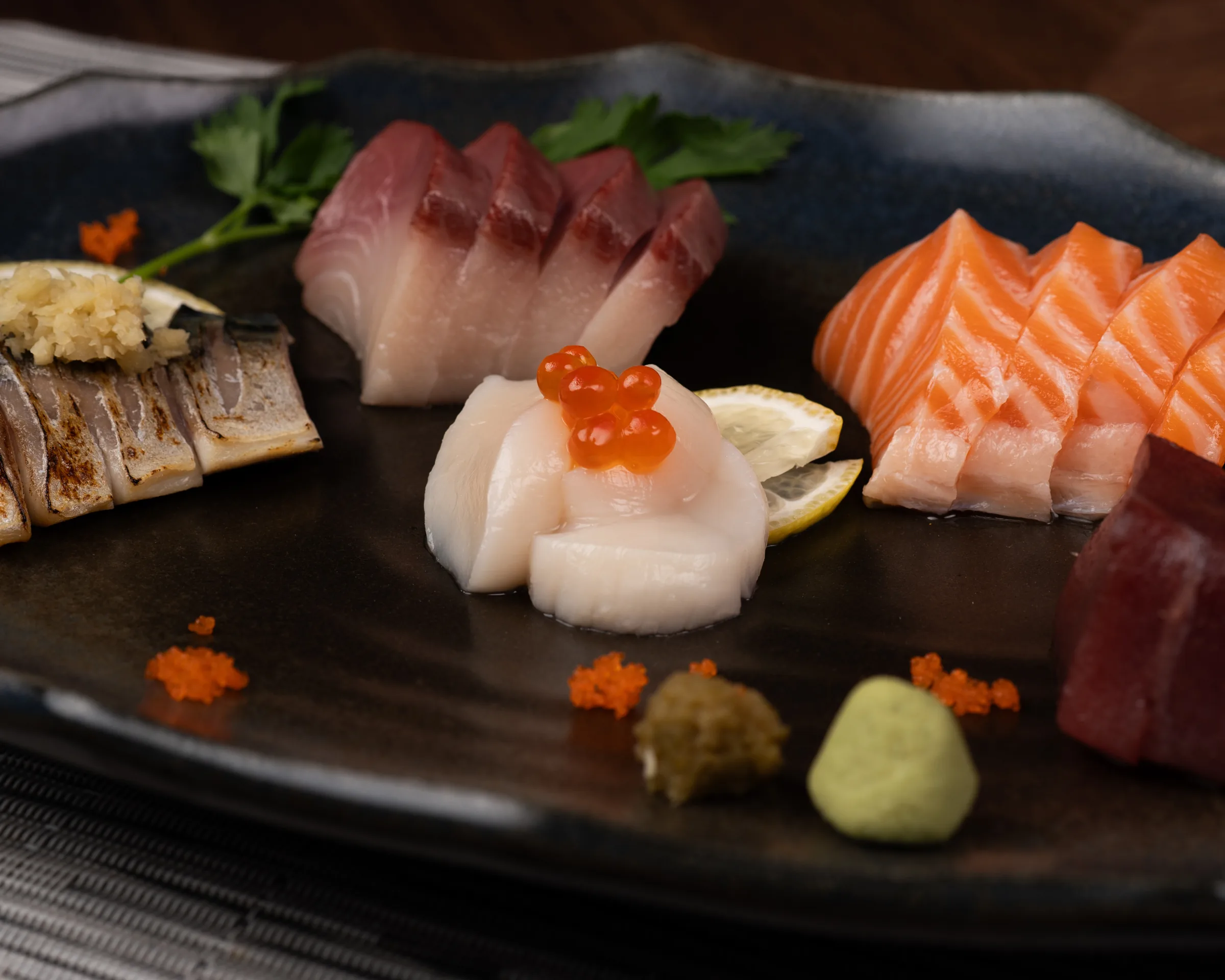 Selección de sashimi y mariscos sobre un plato oscuro.