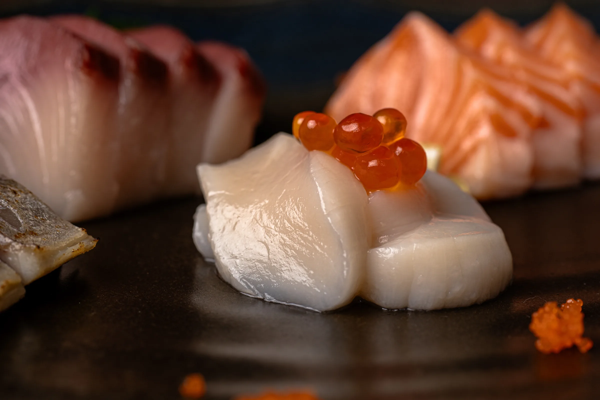 Marisco blanco con huevas anaranjadas y sashimi al fondo.